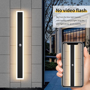 Modern outdoor wall light fixture on a building exterior with a smartphone displaying the product.